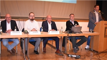 Vier Männer sitzen auf einem Podium, ein Mann steht am Rednerpult. In der Stadthalle Friedeburg in Nordenham ging es um die zukünftige Krankenhauslandschaft in der Wesermarsch.