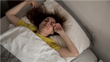 Eine Frau im Bett reibt sich die Augen.