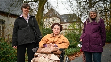 Waltraud Kosak (Mitte) ist mit ihrem Porträt und dem ihres verstorbenen Mannes Erich Teil der Fassade des neuen Traktes des Auswandererhauses. Heute freut sich die 94-Jährige, wenn Tochter Carola (rechts) und Enkelin Bettina sie im Lotte-Lemke-Haus besuchen kommen und eine kleine Runde durch den Park mit ihr drehen. Das Bild entstand vor dem Corona-Lockdown.
