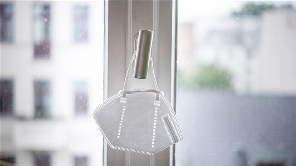 Eine Maske hängt an einem Fenstergriff.