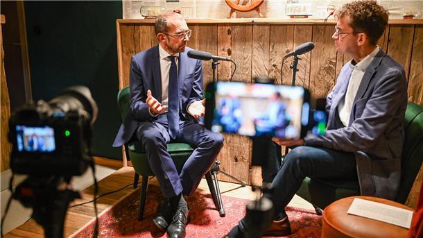 Mann mit Brill gestikuliert mit der Hand und spricht ins Mikrofon.