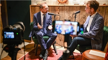 Mann mit Brill gestikuliert mit der Hand und spricht ins Mikrofon.