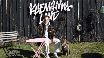 Ein Mann und ein Hund sitzen vor einer Bretterwand, auf der das Wort Kliemannsland steht
