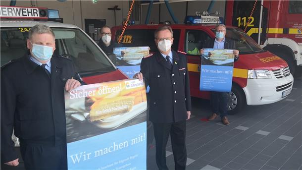 Wenn Geestland Modellkommune wird, könnten diese Plakate bald in den Geschäften und Restaurants hängen – und die örtlichen Feuerwehrhallen zu Testzentren werden. Darauf hoffen (von links): Matthias Witte, Bürgermeister Thorsten Krüger, Friedrich Meyerherm und Henning Dageförde.