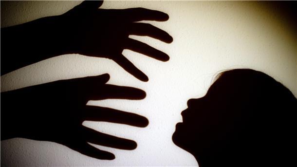 Schatten von Händen einer erwachsenen Person und dem Kopf eines Kindes an einer Wand eines Zimmers