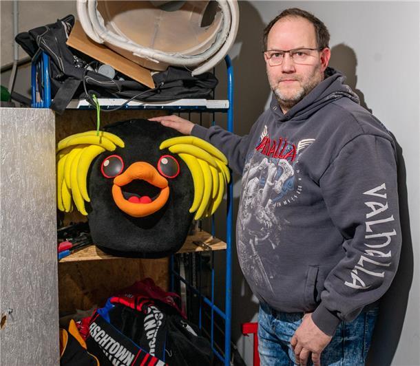 Ein Mann steht neben einem Rollwagen, in dem ein Pinguinkostüm lagert. 