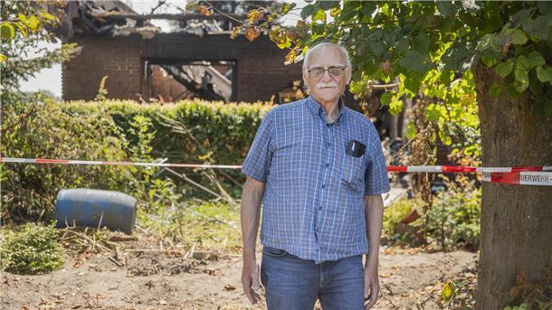 Alter Mann steht vor einem zerstörten Haus.