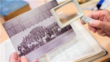  Ein Mann sucht in der Bibliothek des Niedersächsischen Landesvereins für Familienkunde e.V. auf einem historischen Foto nach möglichen Vorfahren. 