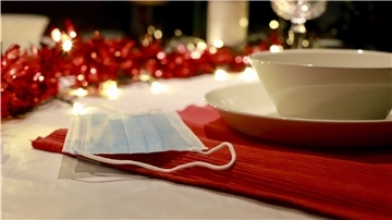 Eine Mund-Nasen-Bedeckung liegt auf einem weihnachtlich gedeckten Tisch.