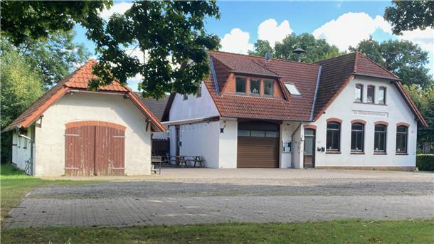 Das aktuelle Feuerwehr- und Dorfgemeinschaftshaus in Kassebruch: Ein weißes Gebäude mit rotem Ziegeldach, daneben ein kleineres Nebengebäude mit Holztoren. Vor dem Haus liegt ein gepflasterter Platz, im Vordergrund eine Rasenfläche.