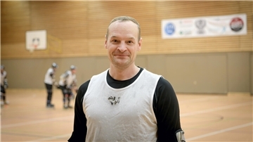 Ein Mann steht auf dem Spielfeld, hinter ihm wird Inline-Skaterhockey gespielt.