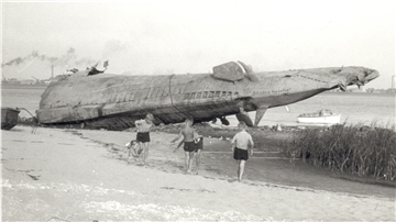 Wie ein abgestürztes Raumschiff liegt es am Strand von Blexen: Das Heck eines deutschen U-Bootes - 1945 von der Besatzung selbst in der Außenweser versenkt, einige Jahre später von mutigen Männern des Schrottwerts wegen wieder geborgen. Kinder spielen davor - ein Bild, in dem sich die 50er Jahre des Nachkriegsdeutschlands verdichten. Bei dem Boot dürfte es sich um U 38, ein Boot vom Typ IX A, gehandelt haben - 1938 in Dienst gestellt und 1.032 Tonnen schwer. Das Foto entstand im August 1955.
