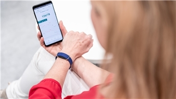 Model Anne Apitzsch präsentiert ein Smartphone mit der App für den tragbaren Blutdruckmesser.