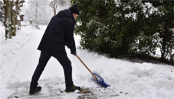 Ein Mann schaufelt Schnee mit einem Schneeschieber.