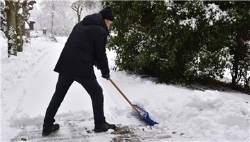 Ein Mann schaufelt Schnee mit einem Schneeschieber.