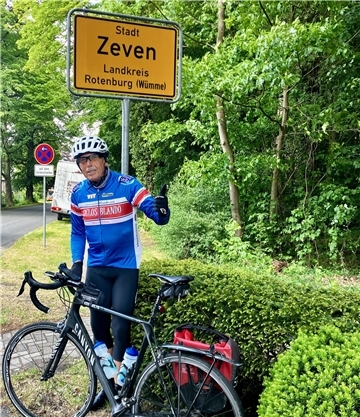 Ein Mann mit einem Rennrad vor einem Ortsschild.