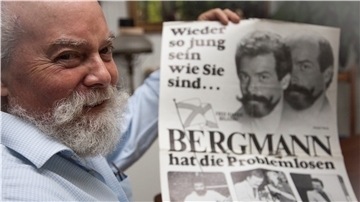 Wilhelm Schaawé hält ein Plakat aus früheren Zeiten hoch. Es zeigt ihn als Toupetmodel.