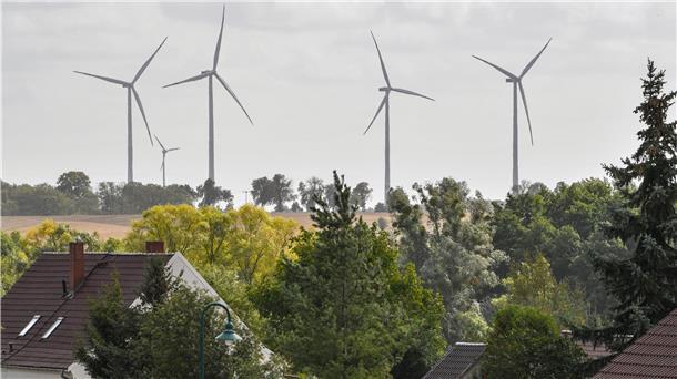 Windenergieanlagen stehen auf einem Feld unweit von Einfamilienhäusern entfernt.