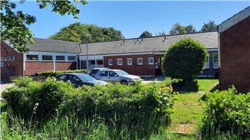 Ein Schulgebäude von außen, davor Büsche, Autos und Gras.