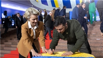 Wolodymyr Selenskyj und Ursula von der Leyen schreiben ihre Wünsche auf eine ukrainische Flagge.