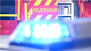 Ein Fahrzeug der Feuerwehr steht bei einem Einsatz auf einer Straße, während im Vordergrund das Blaulicht eines Polizeifahrzeugs zu sehen ist.