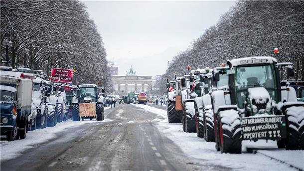 Zahlreiche schneebedeckte Traktoren stehen auf der Straße des 17. Juni vor dem Brandenburger Tor in Berlin.