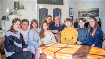 Die Familien sitzen gemeinsam an einem Tisch und blicken in die Kamera.