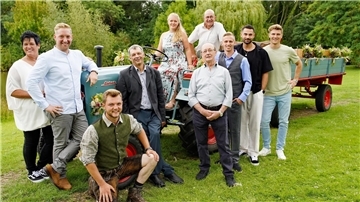 Menschen stehen um einen Traktor im Freien herum, zwei sitzen drauf.