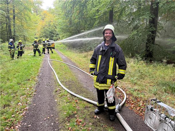 Lachender Feuerwehrmann im Wald, dahinter Feuerwehrleute mit Schläuchen