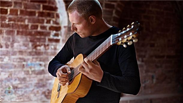 Ein Mann spielt Gitarre, im Hintergrund ist eine geklinkerte Mauer zu sehen. Der Musiker tritt am Sonntag bei einer Veranstaltung der Musikschule Wesermarsch auf.