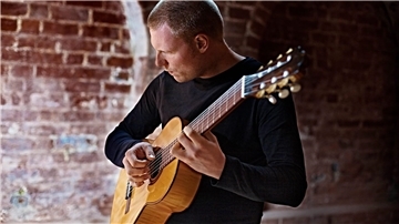 Ein Mann spielt Gitarre, im Hintergrund ist eine geklinkerte Mauer zu sehen. Der Musiker tritt am Sonntag bei einer Veranstaltung der Musikschule Wesermarsch auf.