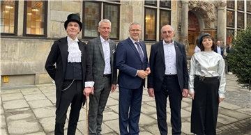 Fünf Menschen, drei in Anzügen, und zwei in Kostümen, stehen vor dem Gewerbehaus der Handwerkskammer Bremen am Ansgarikirchhof.