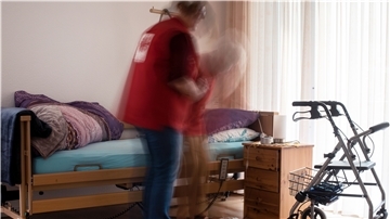 Eine Pflegerin hilft einer alten Frau beim Aufstehen aus ihrem Bett.