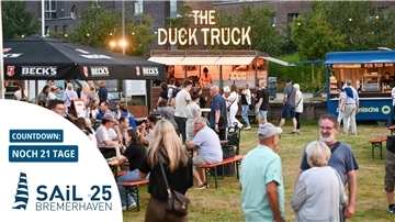 Viele Menschen schlendern über ein Streetfood-Festival auf einer Grünfläche.