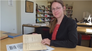 Eine Frau sitzt an einem Tisch und hat ein Heftaufgeschlagen