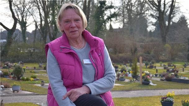 Karin Miosga sitzt auf einem der Bänke des Friedhofs in Atens. Im Hintergrund sind die Gräber zu sehen. 
