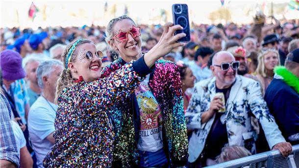 Elton John lässt sich in Glastonbury feiern Zwei Festivalbesucherinnen in glitzernden Jacken und Sonnenbrillen.