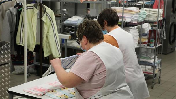 Weniger Arbeitslose mit Handicap - nur kurze Erholung? Zwei Frauen arbeiten in der Wäscherei der Lebenshilfe Gera e.V und legen dort Wäsche zusammen.