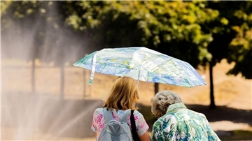 Zwei Frauen schützen mit einem Regenschirm vor der Sonne.