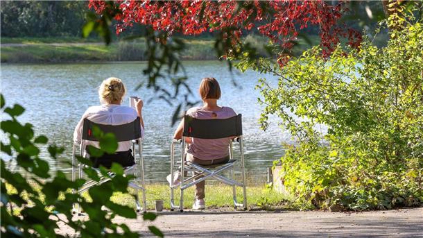 Heiteres und trockenes Wetter in der neuen Woche Zwei Frauen sitzen im baden-württembergischen Ertingen an einem See in der Sonne.