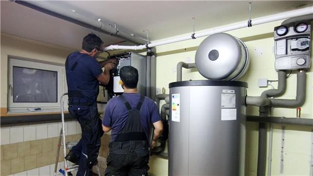 Blick in den Keller: Wie wird die Heizung klimaneutral? Zwei Handwerker stellen eine gerade installierte Wärmepumpe im Keller einer Doppelhaushälfte ein.