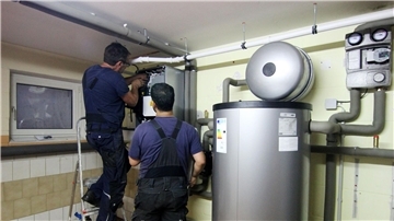 Zwei Handwerker stellen eine gerade installierte Wärmepumpe im Keller einer Doppelhaushälfte ein.
