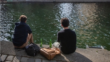Zwei junge Männer trinken am Ufer des Kanals Saint-Martin gemeinsam Bier.