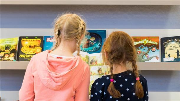Zwei Mädchen stehen bei der „Kibum“ (Kinder- und Jugendbuchmesse) in der Stadtbibliothek PFL.