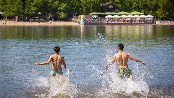 Zwei Männer rennen in einen Badesee. 