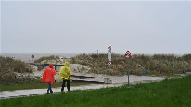 Küste bereit für Saisonstar: Strandkörbe kommen ins Freie Zwei Tagesgäste laufen bei nassem Wetter in Regenjacken an der Starndpromenade entlang.