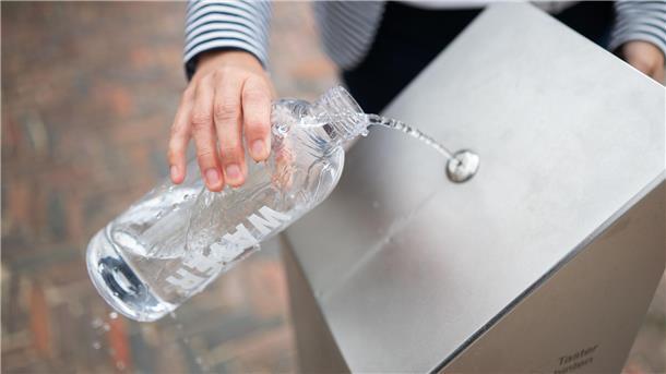 Eine Flasche wird an eine Trinkwasser-Zapfstelle gehalten 